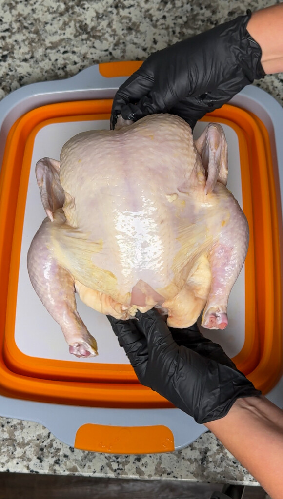 a raw chicken being held by a black gloved hand over a white board