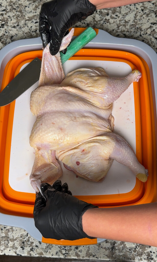 a raw flattened spactchcock chicken on a white and orage board