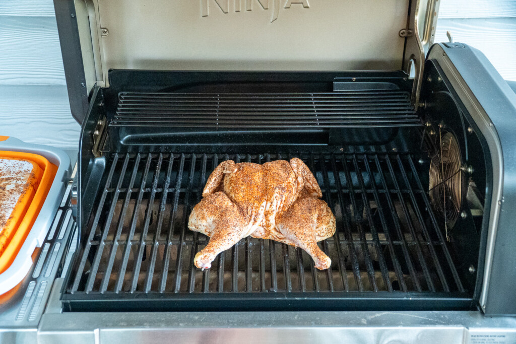 a raw seasoned spatchcock chicken on the grill