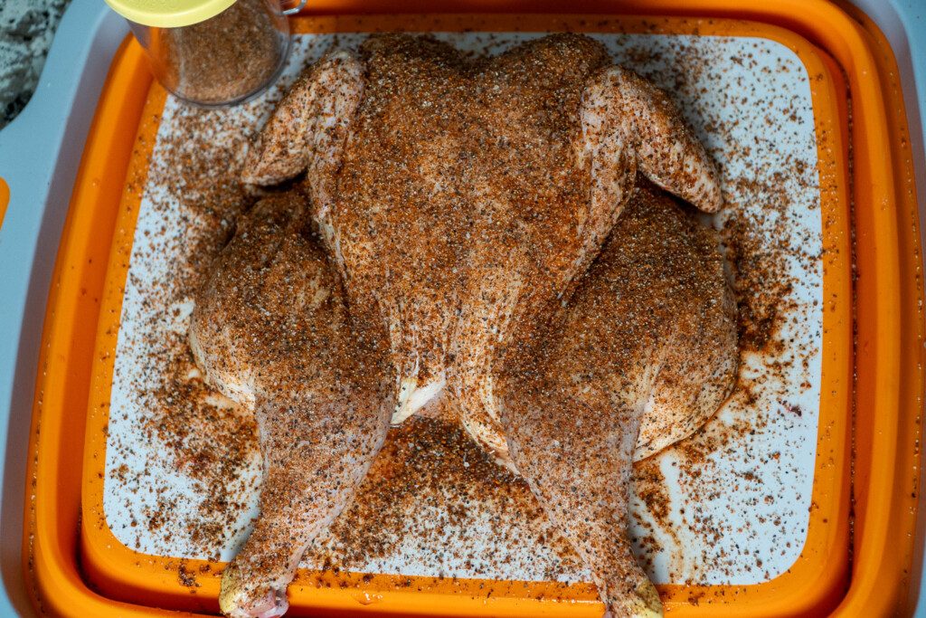 a raw seasoned spatchcock chicken on a white board