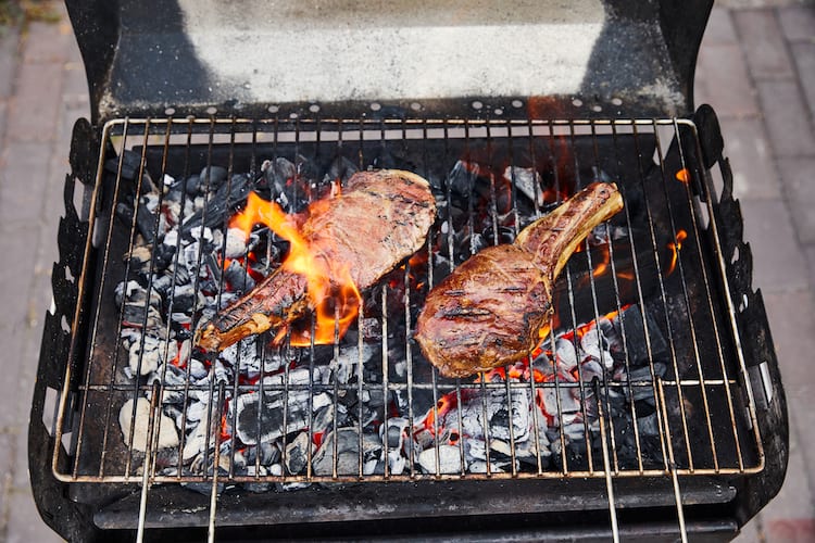 steaks grilling with fire flare-ups on a small charcoal grill