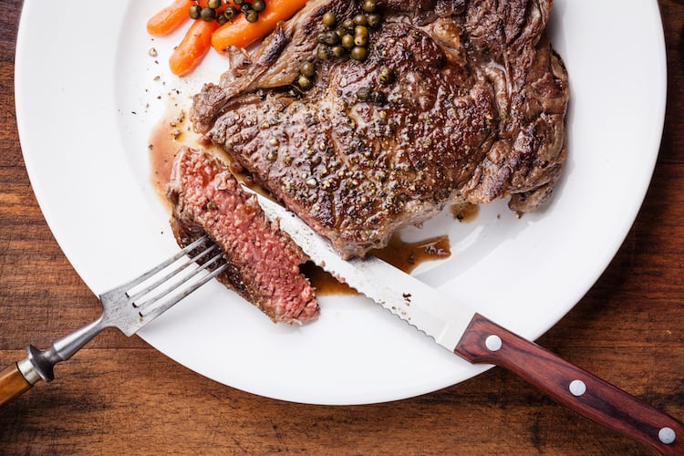 A piece of cooked meat on a white plate along with a fork and a knife