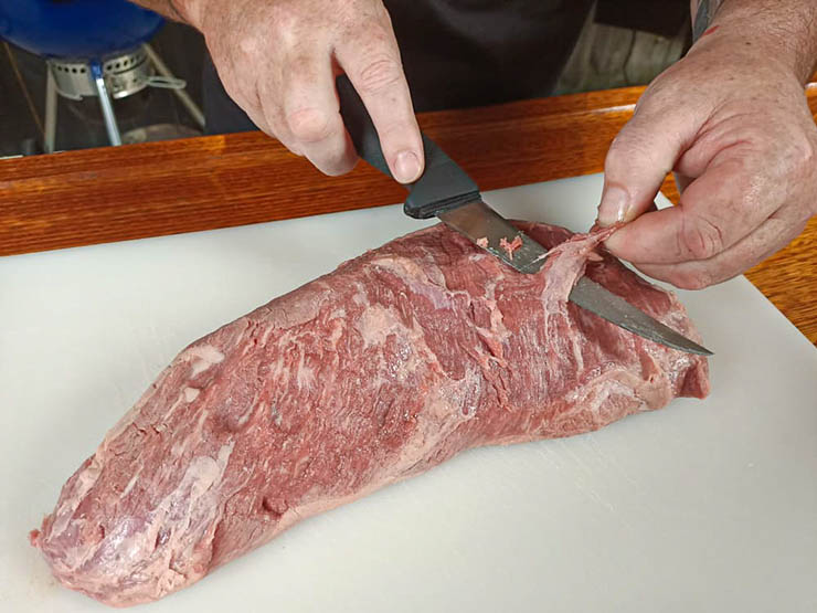 a man trimming a tri tip with a knife