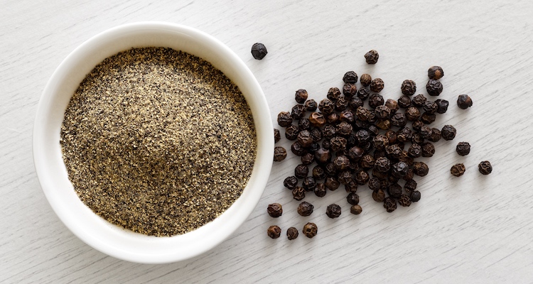ground black pepper in a bowl with peppercorns on a side