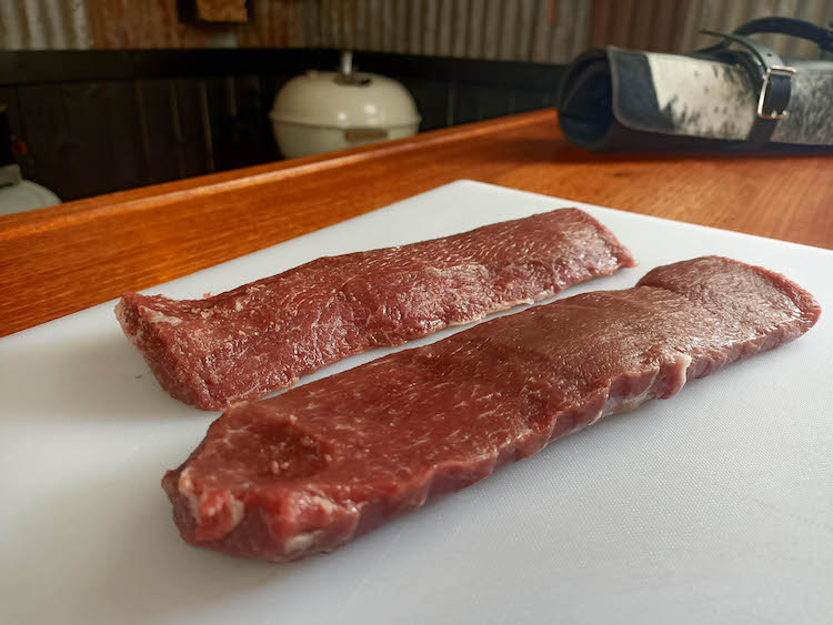 two uncooked lamb backstraps on a white cutting board