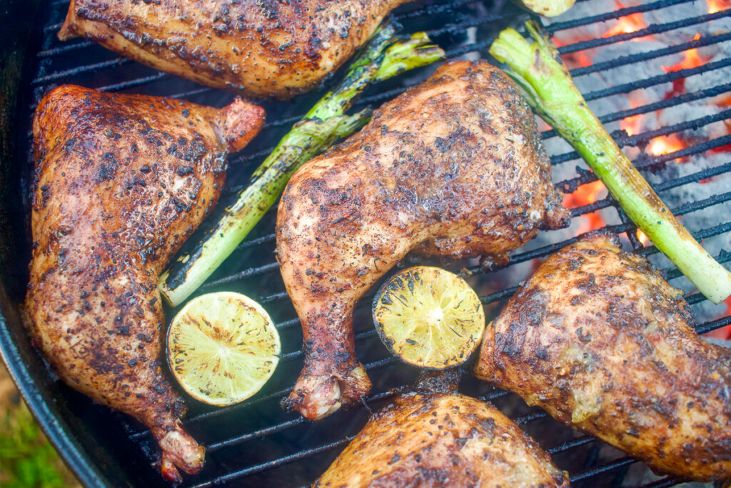 chicken quarters, lime halves and onions on the grill with glowing charcoal underneath