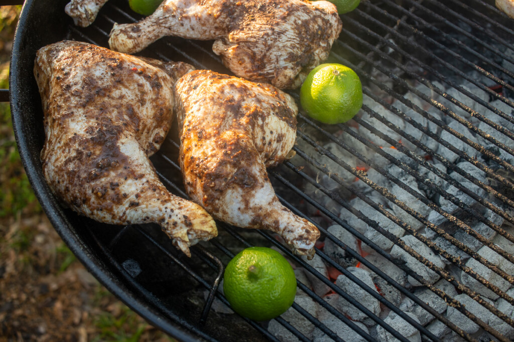 chicken quarters with jerk marainade and lime halves moved to the side of the grill