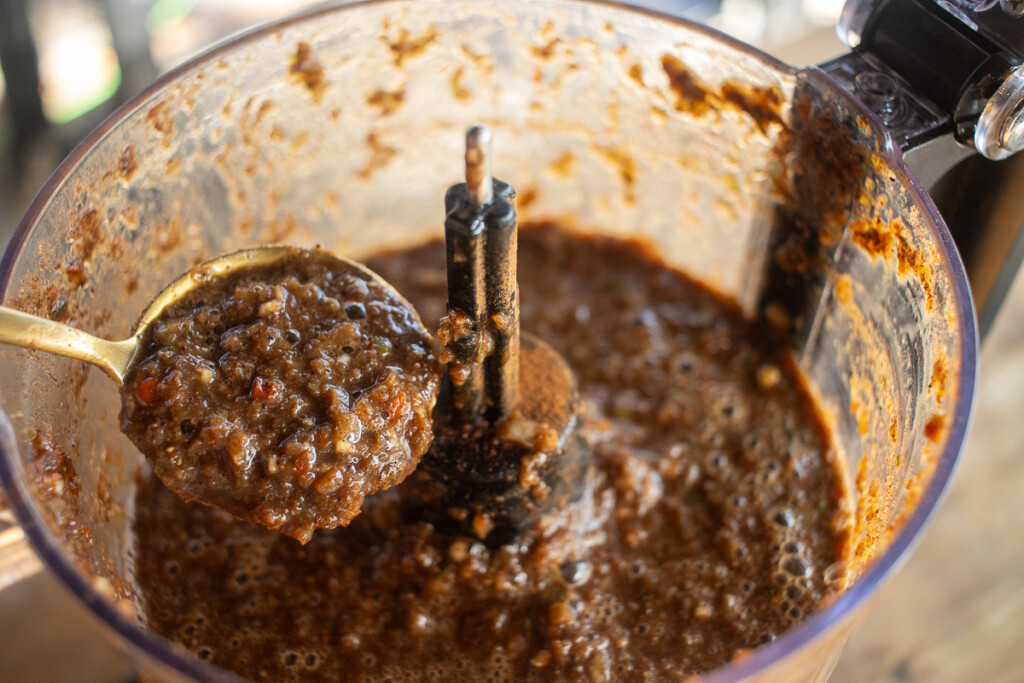 a food processor with the whizzed up jerk marinade, and a spoonful being held up