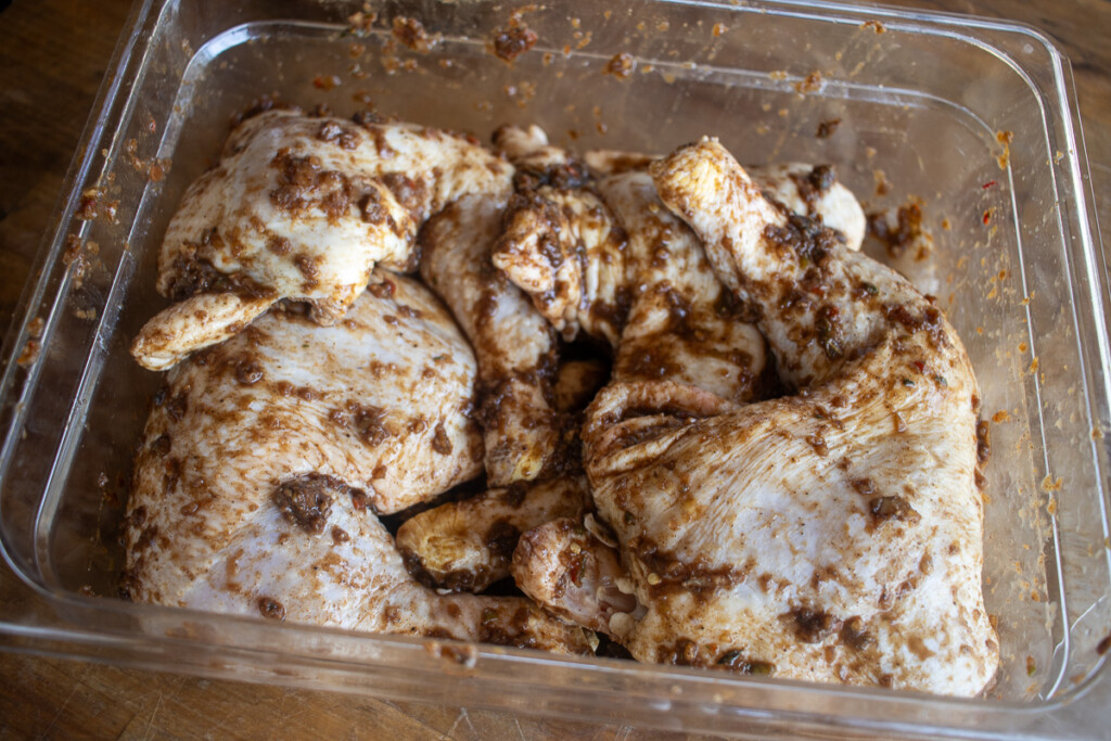raw chicken quarters covered in jerk marinade in a plastic container