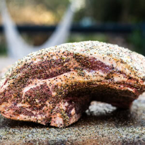 Seasoned raw lamb shoulder coated in a herb and pepper rub on a cutting board.