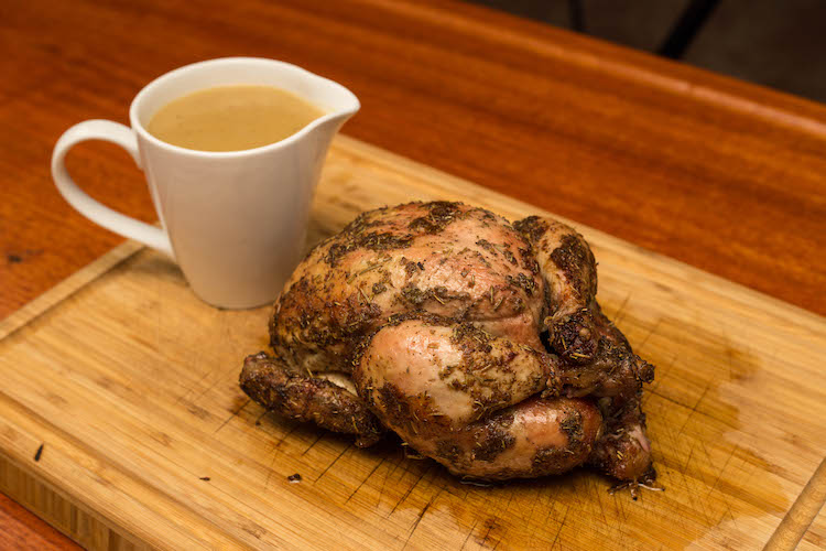 rotisserie chicken and a sauce boat with gravy on a wooden board