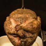 whole chicken on a rotisserie cooking over charcoal