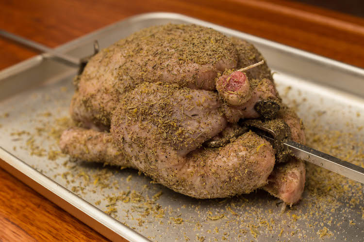 uncooked whole chicken on a rotisserie seasoned with herbs