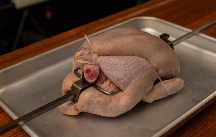 uncooked whole chicken tied with a butcher's twine on a rotisserie
