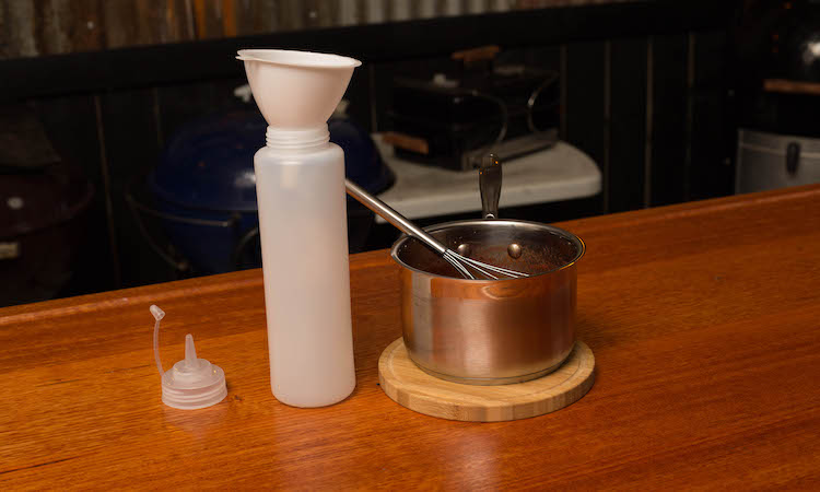 BBQ sauce in a saucepan and a sauce bottle on a wooden table