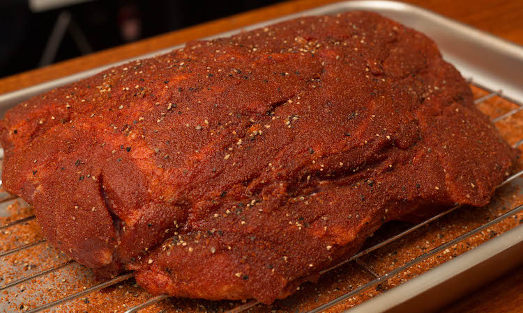 raw pork butt covered in pork rub on a metal tray