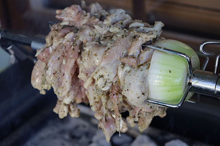 raw pieces of chicken and half an onion on a rotisserie rod