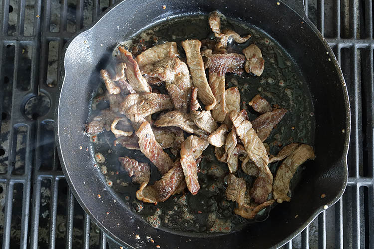 steak slices cooking on a cast iron skillet