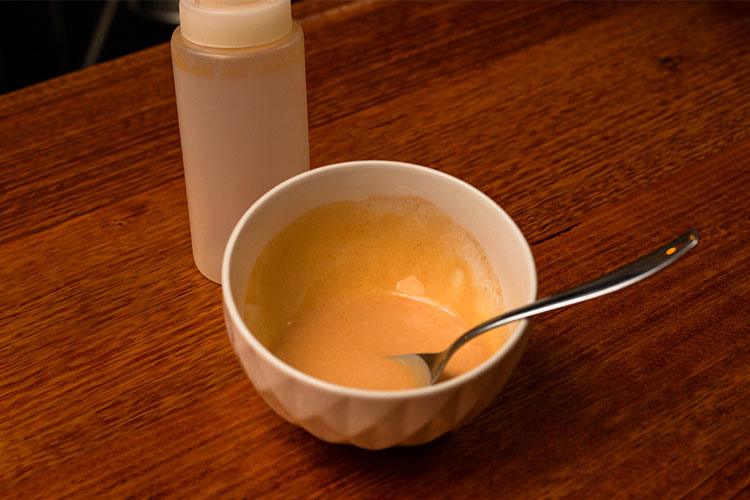 a bowl of creamy hot sauce and an empty sauce bottle on a wooden table