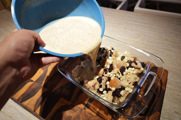 pouring cream, eggs and spices mixture on top of hot cross buns for the bread pudding