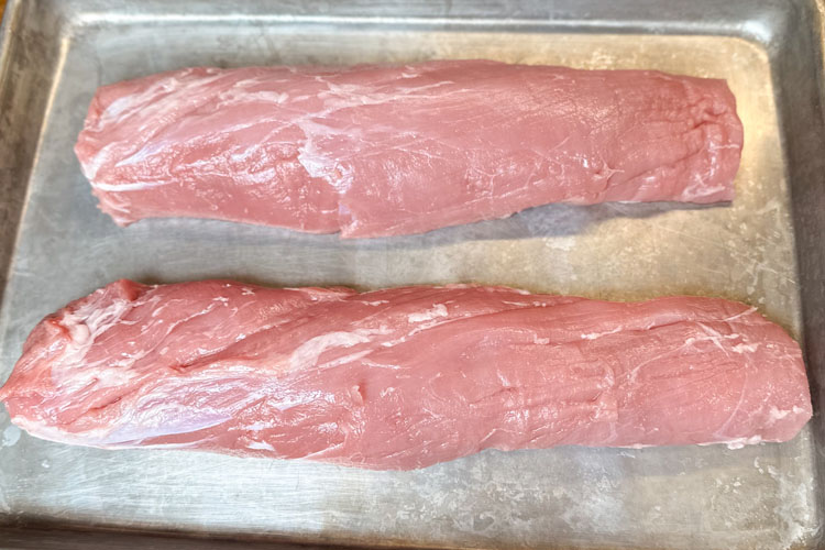 two raw tenderloins on a silver sheet pan