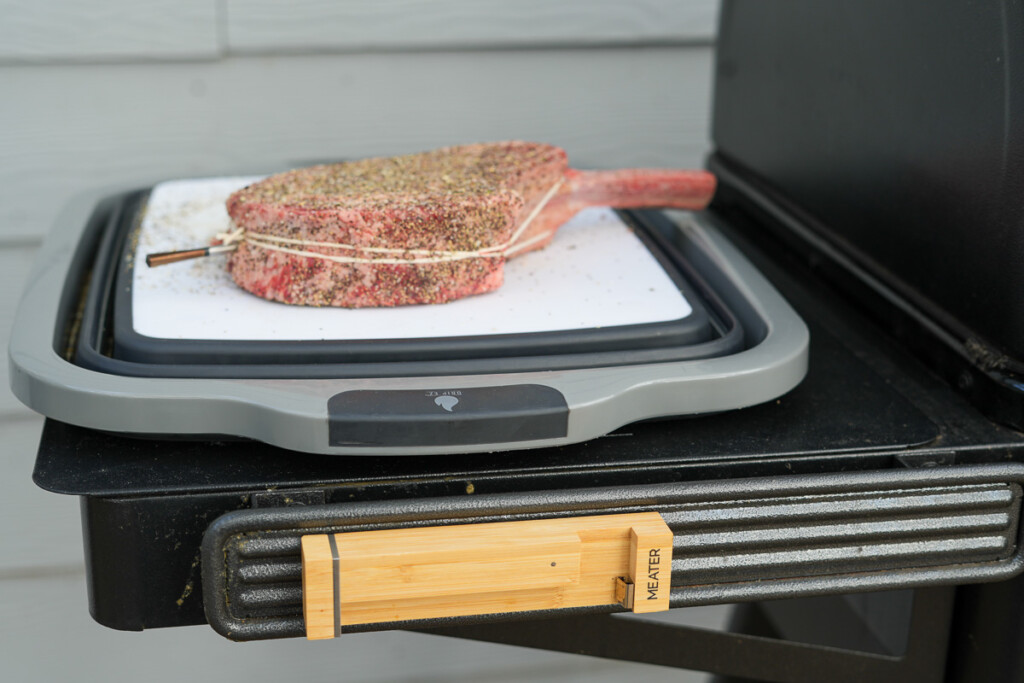 a raw tomakawk steak on a white board with a meater thermometer stuck in it
