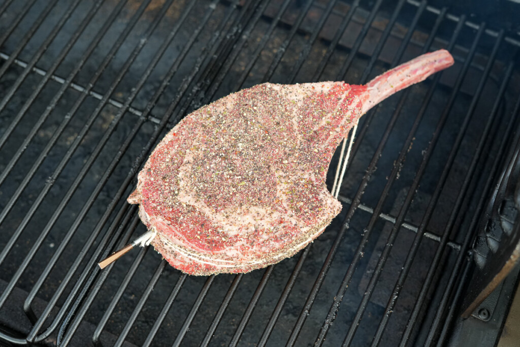 a raw tomahawk steak on the smoker