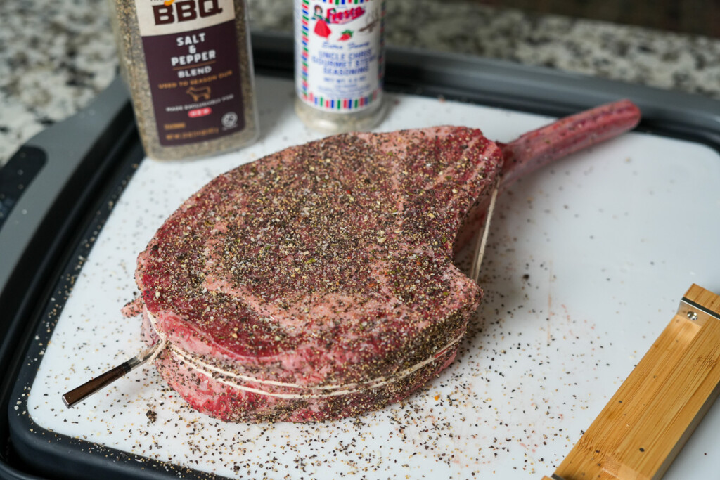 a raw seasoned tomahawk steak on a white board