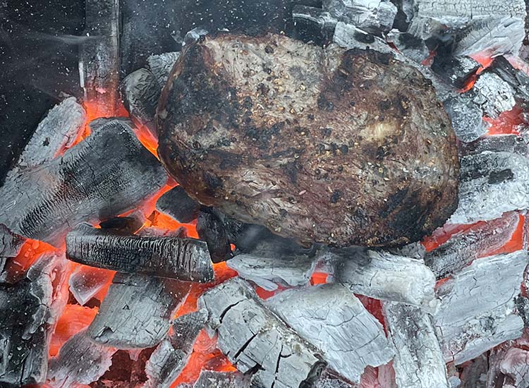 cooked caveman ribeye steak on hot lump charcoal
