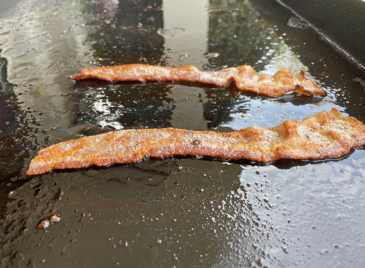 bacon strips cooking on a griddle