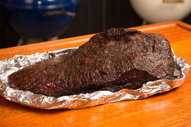 beef brisket boated in foil on a wooden table 