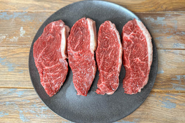 four pieces of raw steak on a black plate