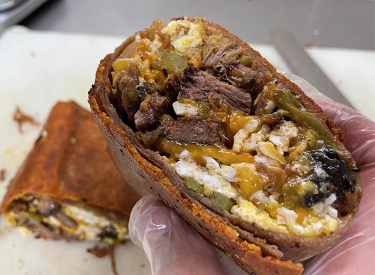 a man holding a half of brisket breakfast burrito