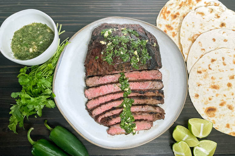 carne asada slice on a white plate with serving condiments around it
