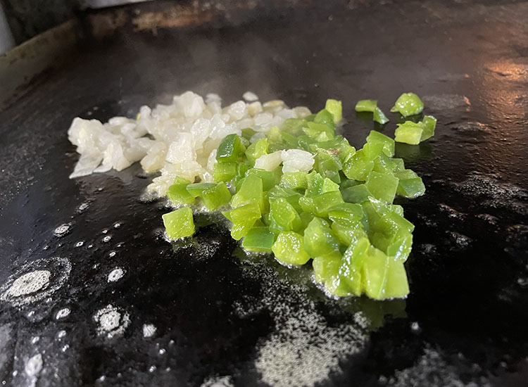 chopped onion and bell pepper on a griddle