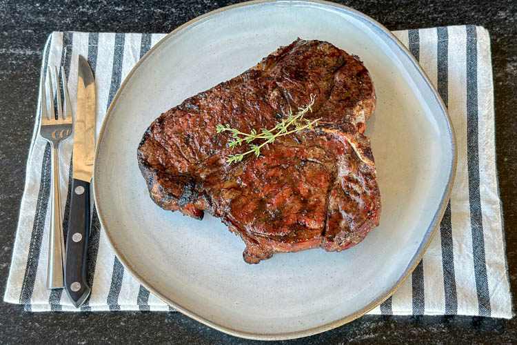 cooked porterhouse steak on a white plate and striped napkin