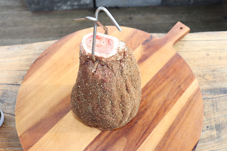 beef shank covered in rub sitting on a wooden chopping board