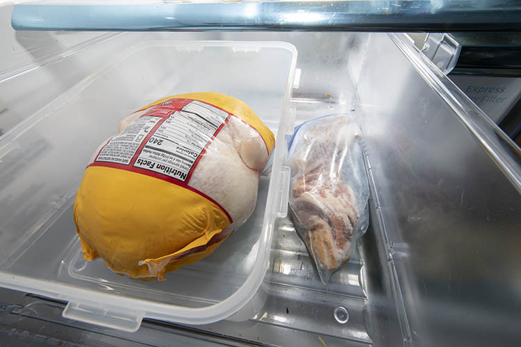A whole chicken in a sealed package thaws in a tray in the fridge
