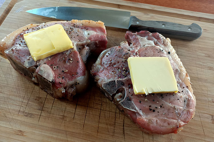 undercooked pork chops with a pices of butter on a wooden board
