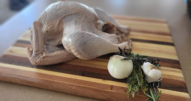 raw turkey on a wooden board with a selection of herbs on the side