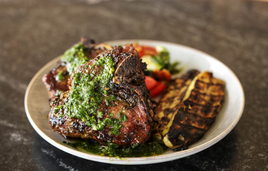 cooked lamb chops with chimichurri on a white plate with grilled veges