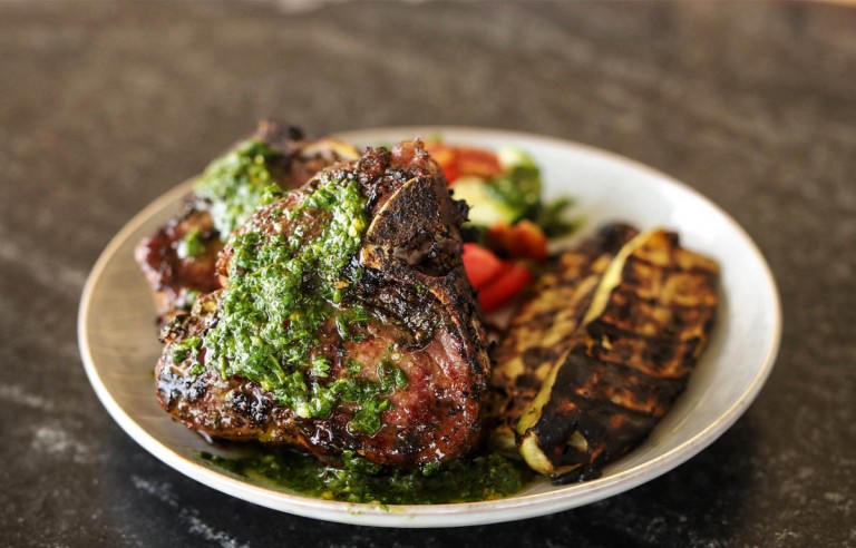 cooked lamb chops with chimichurri on a white plate with grilled veges