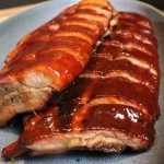 smoked pork ribs slathered in BBQ sauce on a grey plate