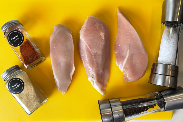 raw chicken on yellow board with jars of seasoning