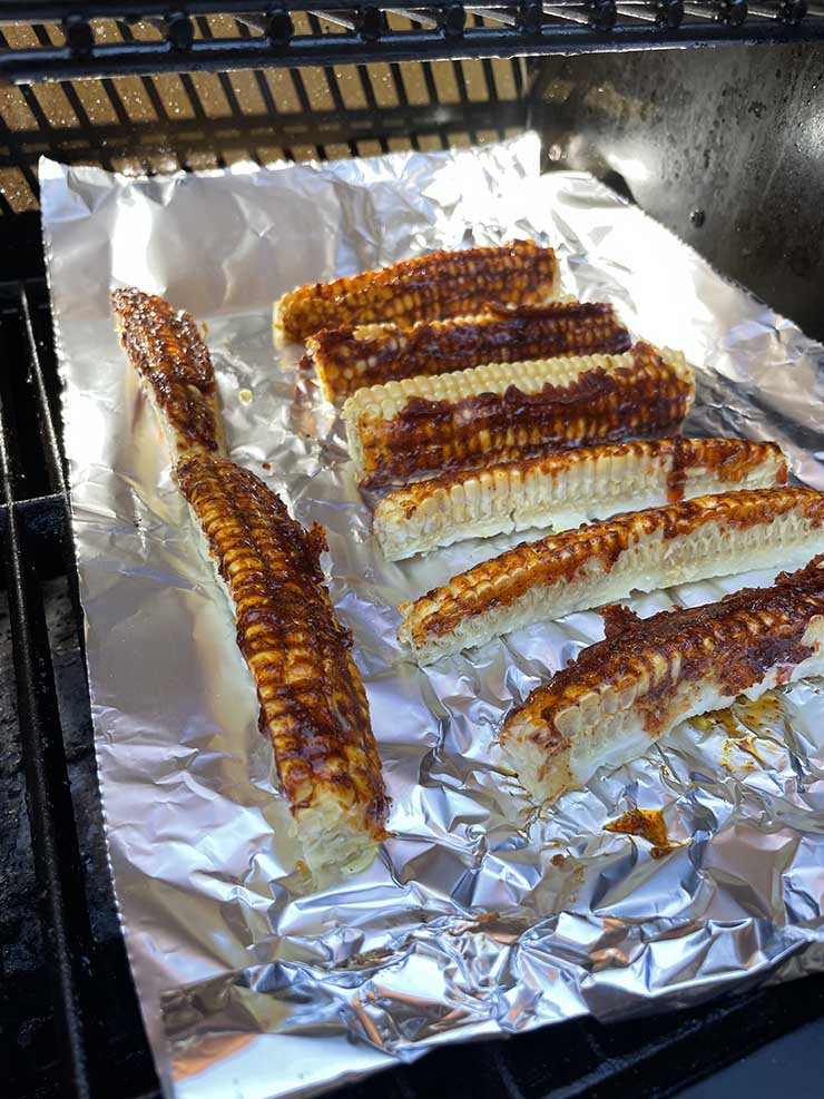 corn ribs covered in wet rub on a baking tray in the smoker