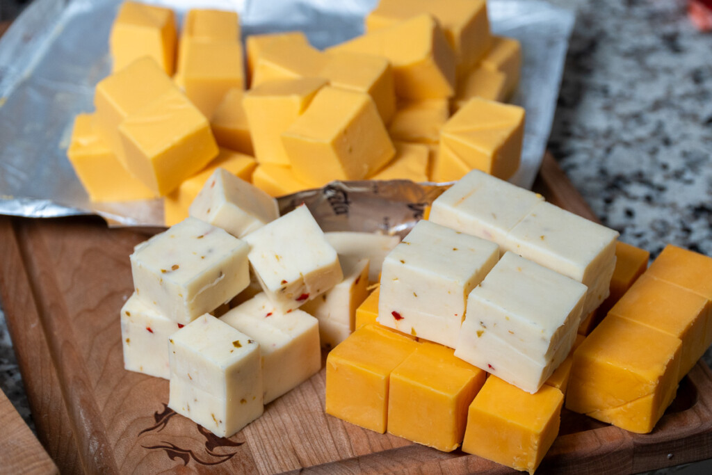 cubed, cheddar, pepper jack and velveeta cheese on a wooden board