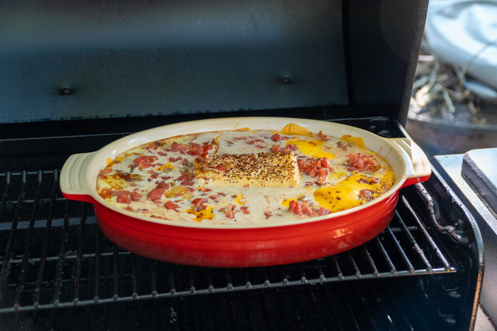 a red dish with melting queso dip ingredients in it on the smoker