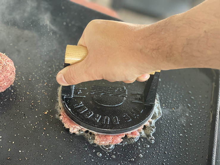 burger smasher tool on top of a beef patty on a griddle
