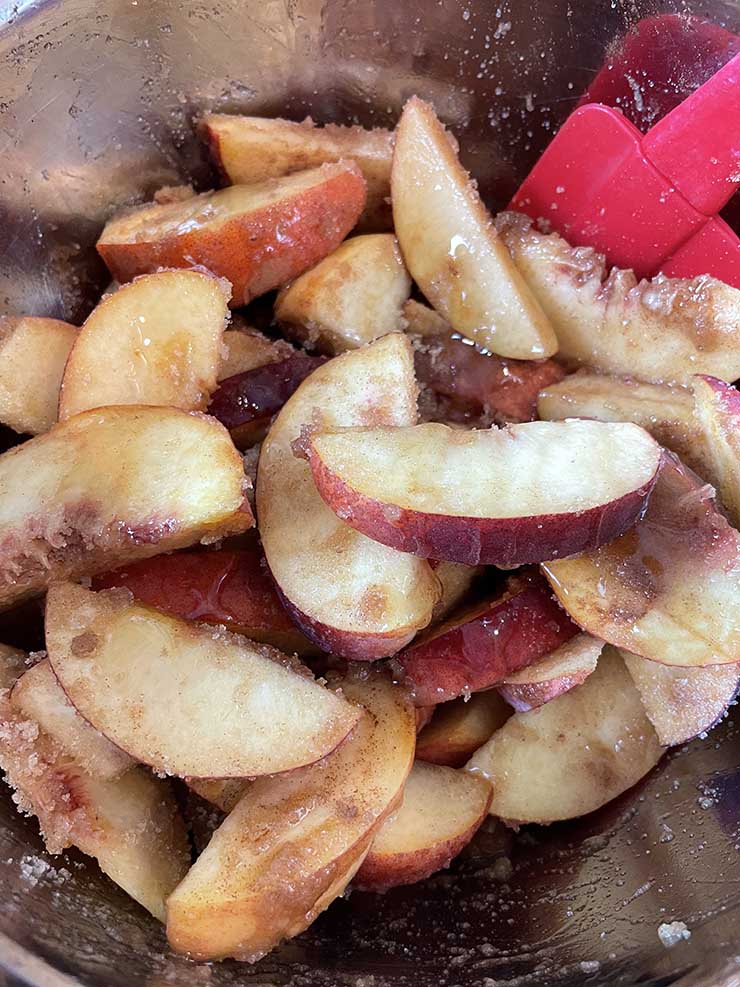 peach slices covered in sugar and agave nectar mix in a metal bowl
