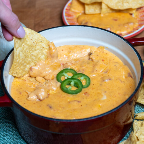 smoked queso dip in a serving dish with a tortilla being dunked in it.